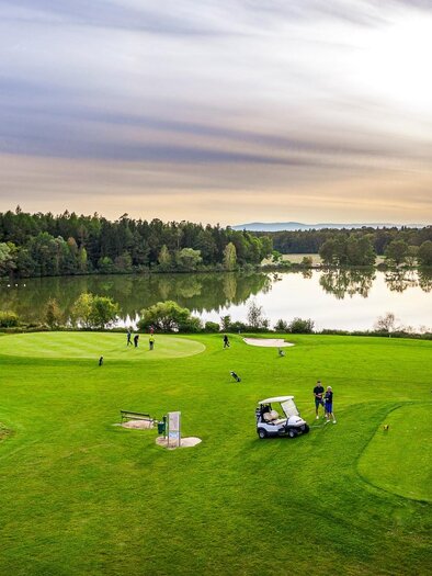 A picturesque golf course with green fairways and a lake in the background. The soft light of the sunset creates a relaxing atmosphere. | © TV- Thermen- & Vulkanland