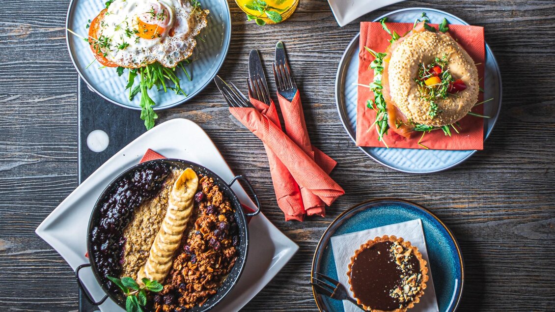 Ein appetitliches Frühstücksangebot mit verschiedenen Gerichten auf Tellern. Dazu ein Getränk in einem Glas und Besteck. | © Granola