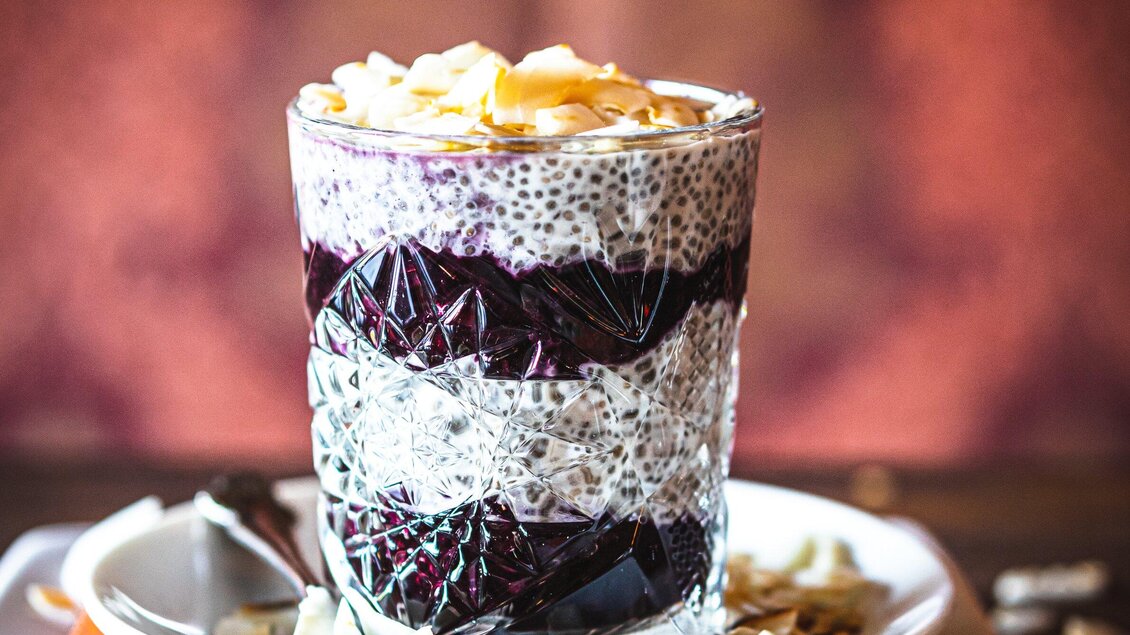 Ein Glas mit Schichtdessert, das Chiasamen und Beeren enthält. Oben ist es mit gerösteten Mandeln dekoriert. | © Granola