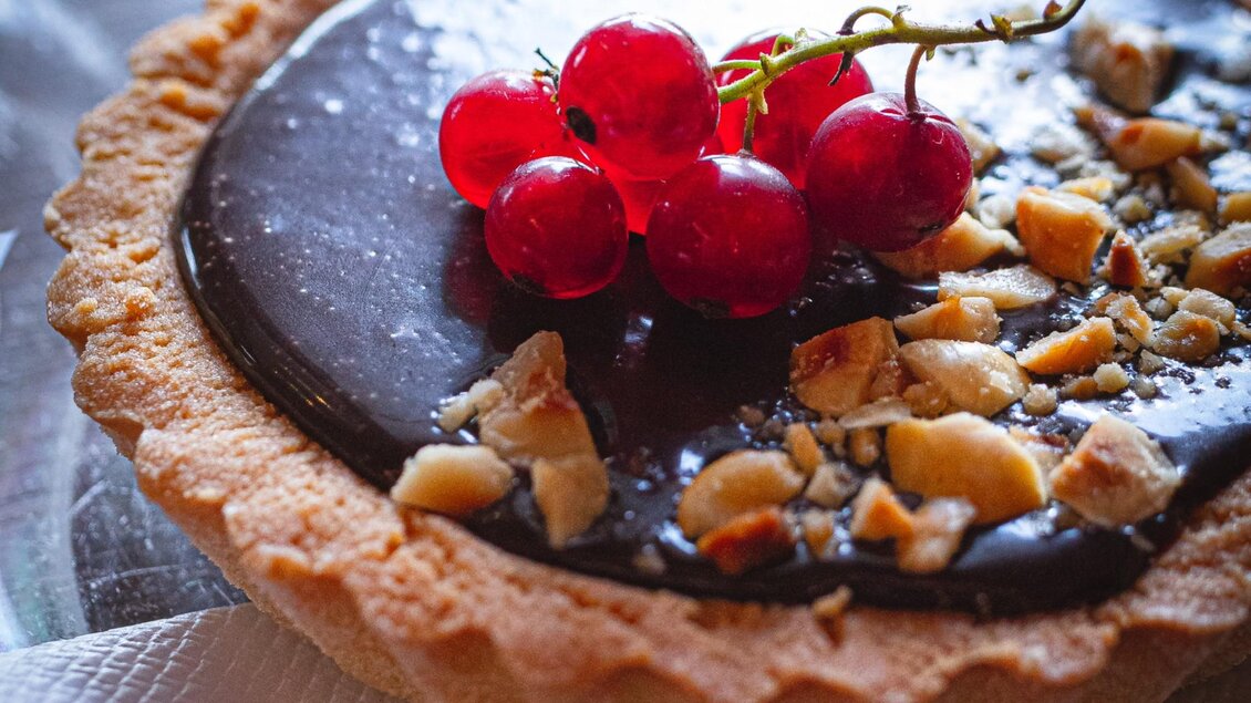 Eine köstliche Torte mit einer Schokoladenschicht und einer Dekoration aus roten Johannisbeeren. Die Torte ist mit gehackten Nüssen bestreut. | © Granola