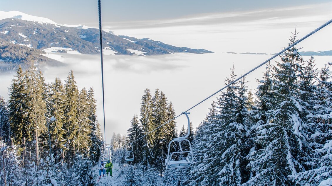 Eine malerische Winterlandschaft mit verschneiten Bäumen und einer Seilbahn. Im Hintergrund sind schneebedeckte Berge und Nebel sichtbar. | © Gaaler Skilifte