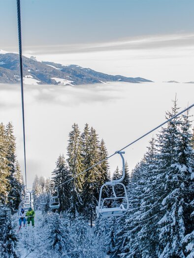 A picturesque winter landscape with snow-covered trees and a cable car. In the background, snow-covered mountains and mist are visible. | © Gaaler Skilifte
