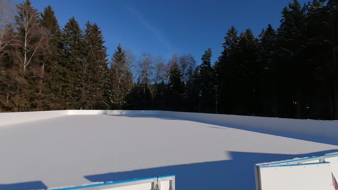 Eine leere Eislauffläche umgeben von schneebedeckten Bäumen. Der Himmel ist klar und blau. | © Häuserl im Wald