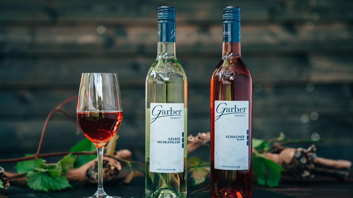 Zwei Flaschen Wein stehen neben einem gefüllten Glas. Im Hintergrund sind Weintrauben und Blätter zu sehen. | © Gaber Patrick Weine