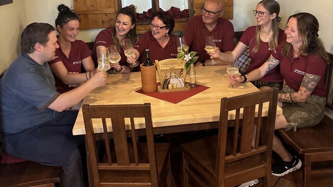 Eine Gruppe von Menschen sitzt um einen Tisch und prostet mit Getränken. Alle tragen einheitliche T-Shirts und wirken fröhlich. | © Gasthaus Ägydi