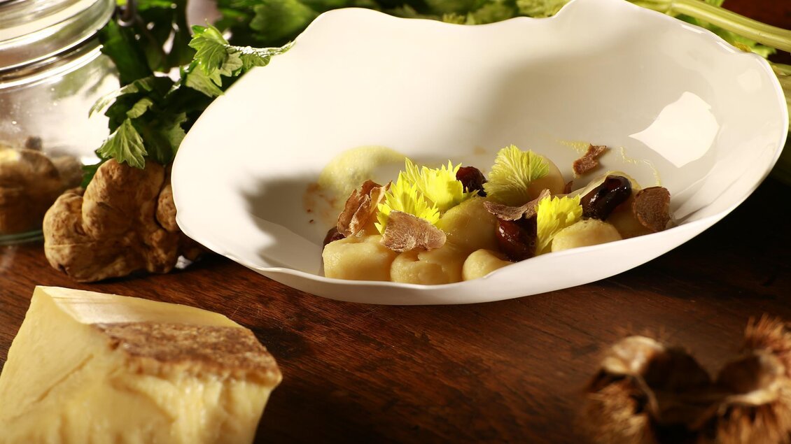 Ein elegantes Gericht auf einem weißen Teller, garniert mit frischen Kräutern und essbaren Blüten. Verschiedene Zutaten wie Gnocchi und Pilze sind kunstvoll angerichtet. | © Gasthaus Thaller