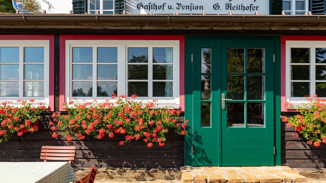 Ein typisches Gasthaus mit einer grünen Tür und weißen Fenstern. Bunte Blumen schmücken die Fensterbank. | © TV Region Graz - Harry Schiffer