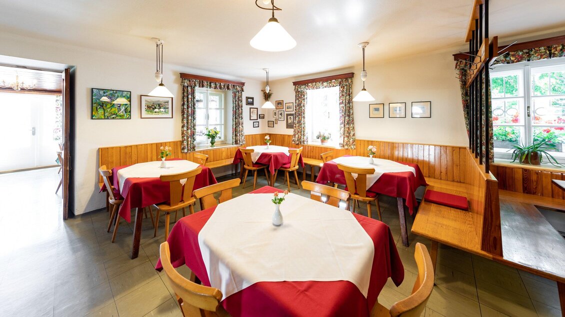 Ein gemütlicher Raum mit Holzverkleidung und roten Tischdecken. An den Tischen stehen Blumenvasen, und an den Wänden hängen Bilder. | © TV Region Graz - Harry Schiffer