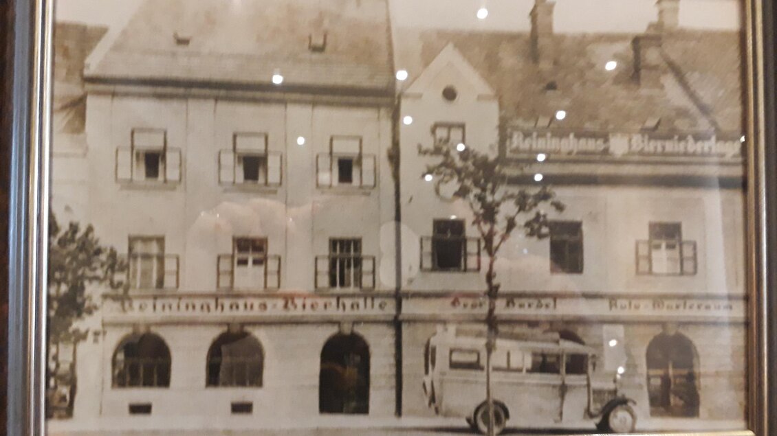 Ein historisches Foto eines Gebäudes mit großen Fenstern und einem Baum im Vordergrund. Ein Oldtimer-Auto ist ebenfalls sichtbar, was die nostalgische Atmosphäre verstärkt. | © TV Lipizzanerheimat