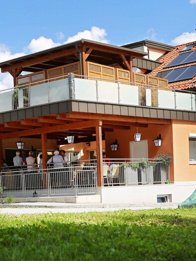 A modern house with a large balcony and a green slide in the garden. Several people are gathered outdoors. | © TV Region Graz - Lunghammer