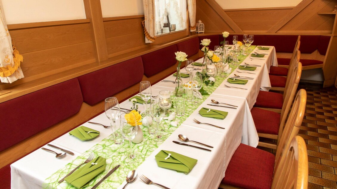 Ein festlich gedeckter Tisch mit weißer Tischdecke und grüner Dekoration. Das Arrangement umfasst Blumen, Gläser und Besteck, perfekt für eine Veranstaltung. | © TV Region Graz - Lunghammer