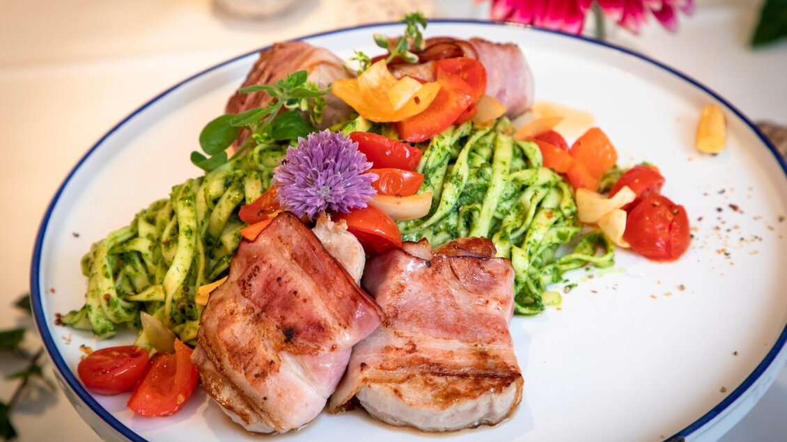 Ein Teller mit gegrilltem Fleisch, umwickelt mit Speck, und einem bunten Gemüsesalat. Dazu gibt es frische grüne Nudel mit Tomaten und Kräutern. | © TV Region Graz - Lunghammer