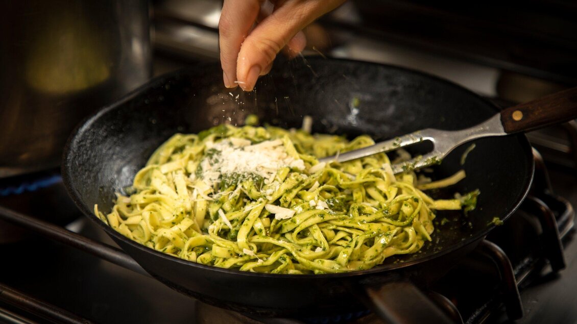 Ein Koch hält eine Hand über eine Pfanne mit frischen Nudeln. Er streut Käse über die Nudeln in der heißen Pfanne. | © TV Region Graz - Lunghammer