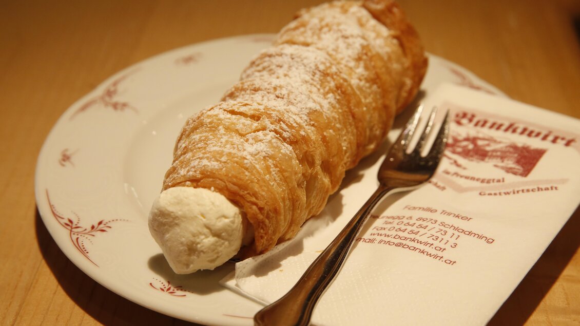 Ein köstliches Dessert auf einem weißen Teller. Es handelt sich um eine cremige Rolle, bestäubt mit Puderzucker. | © Herbert Raffalt