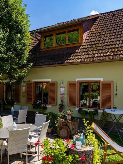 Ein gemütliches Café mit einem einladenden Außenbereich. Tische und Stühle stehen unter den Bäumen vor einem charmanten Gebäude. | © TV Region Graz-Harry Schiffer