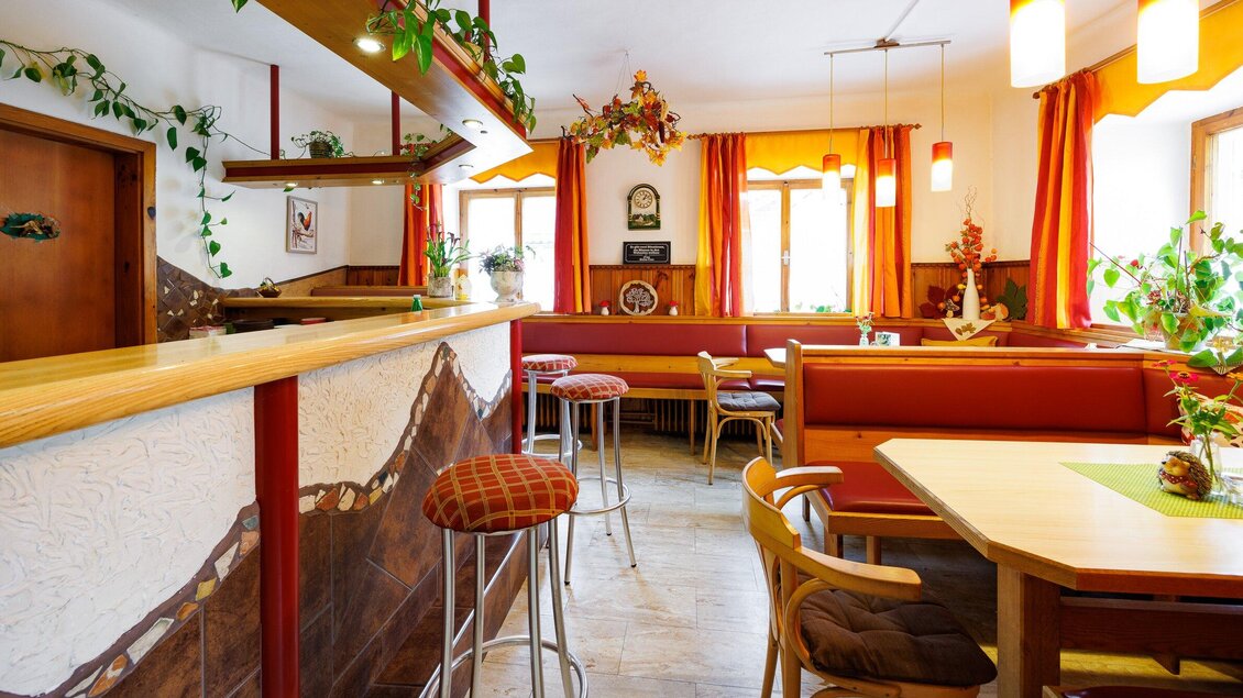 Ein gemütliches Restaurant mit Holzdecor und orangefarbenen Vorhängen. Es gibt eine Bar und mehrere Sitzplätze mit Pflanzen im Hintergrund. | © TV Region Graz-Harry Schiffer
