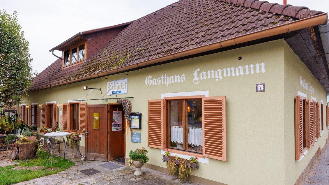 Ein einladendes Gasthaus mit einem hellen Außenanstrich und offenen Fensterläden. Draußen steht ein Tisch, umgeben von Pflanzen, und die Atmosphäre wirkt gemütlich. | © TV Region Graz-Harry Schiffer