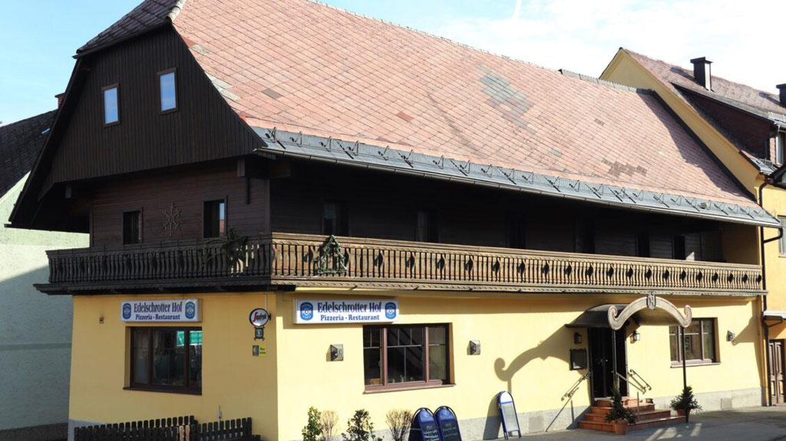 Ein charmantes, zweigeschossiges Gebäude mit einem rot gedeckten Dach. Die Fassade ist gelb, und es gibt einen Balkon sowie ein Restaurantzeichen. | © Steirische Rucksackdörfer
