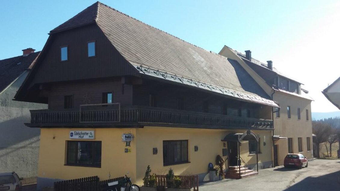 Ein gemütliches Gebäude mit einem breiten Dach und einem Balkon. Die Fassade ist in gelber Farbe gestrichen und es befinden sich Autos auf dem Parkplatz. | © Gemeinde Edelschrott