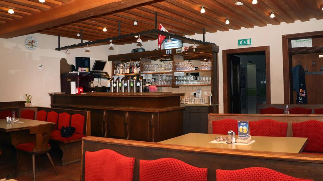 Ein gemütliches Restaurant mit roten Sitzbänken und einem Holzdekor. Die Bar ist gut ausgestattet und bietet eine einladende Atmosphäre. | © Steirische Rucksackdörfer