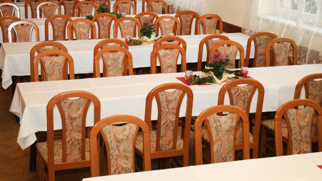 Ein Saal mit mehreren langen Tischen und Holzwarenstühlen. Die Tische sind mit weißen Tischdecken und kleinen Blumen dekoriert. | © Steirische Rucksackdörfer