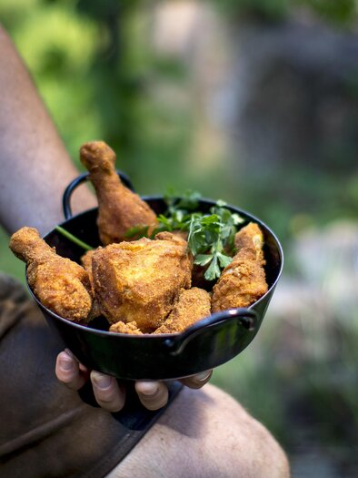A person is holding a bowl of fried chicken and fresh herbs. The background is natural and green. | © Steiermark Tourismus _ Ikarus