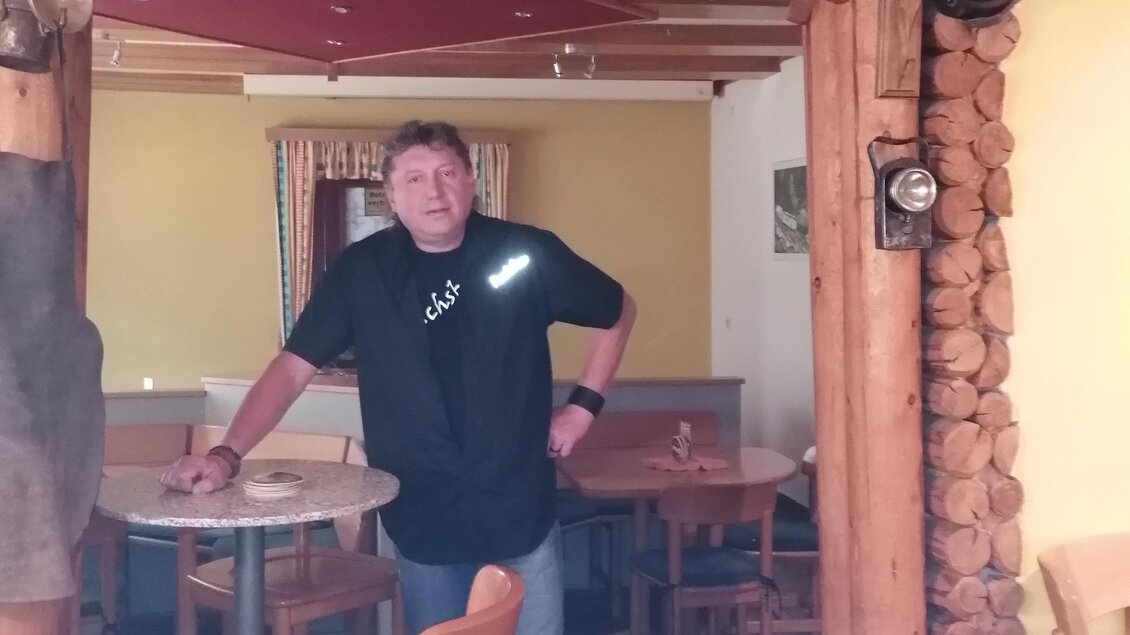 Ein Mann steht an einer Tür mit dem Schild „Glück auf!“ Er ist in einem typisch rustikalen Raum mit Holzvertäfelung und Stühlen. | © Gasthaus Fuchsbau