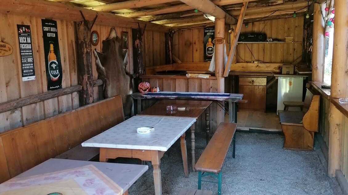 Ein rustikales Holzhaus mit einfachen Tischen und Bänken. Die Einrichtung ist traditionell und gemütlich. | © Gasthaus Fuchsbau