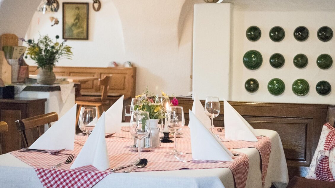 Ein einladendes Restaurant mit einem gedeckten Tisch und traditioneller Dekoration. Die Tischwäsche ist rot-weiß kariert, und im Hintergrund sind grüne Teller ausgestellt. | © Gasthof Gössler