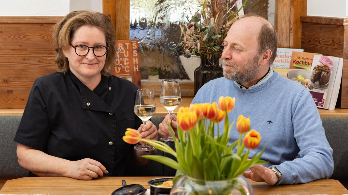 Ein paar genießt in einem gemütlichen Restaurant ein Glas Wein. Auf dem Tisch steht eine Vase mit bunten Tulpen. | © Tv Region Graz-Harry Schiffer