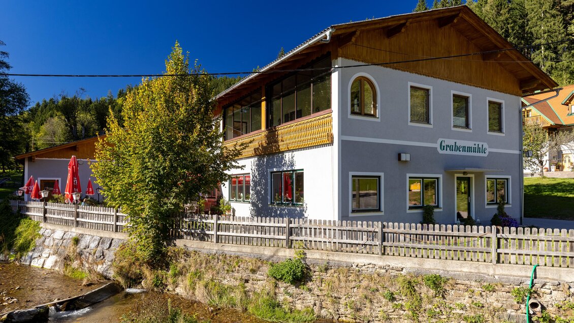 Ein charmantes Gebäude mit einem Holz-Dach in einer ruhigen Umgebung. Neben einem kleinen Fluss umgeben von Bäumen und Grünflächen. | © TV Region Graz | Harry Schiffer