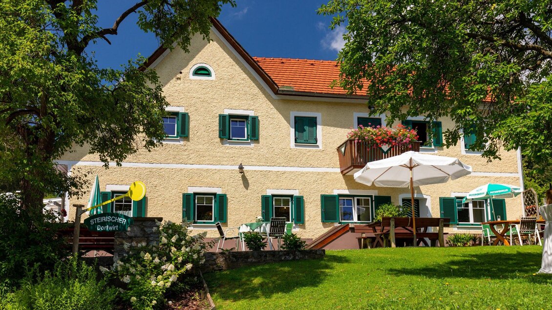 Ein charmantes Haus mit grünen Fensterläden und einem schönen Garten. (Tische und Sonnenschirme laden zum Verweilen ein.) | © TV Region Graz - Harry Schiffer