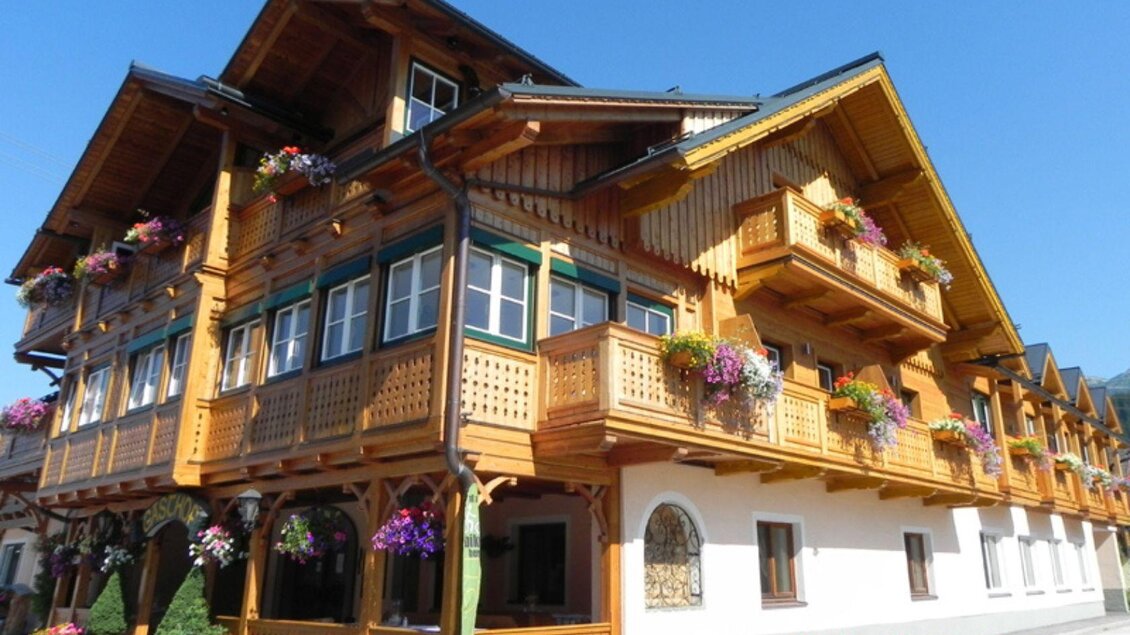 Ein traditionelles alpenländisches Haus aus Holz mit vielen Blumenbalkonen. Die Fassade ist hell und einladend, umgeben von klarem Himmel. | © Landhotel-Restaurant Kanzler