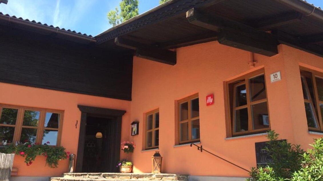 Ein Haus mit einem freundlichen orangefarbenen Anstrich und großen Fenstern. Stufen führen zur Eingangstür, umgeben von Pflanzen. | © Familie Koschak