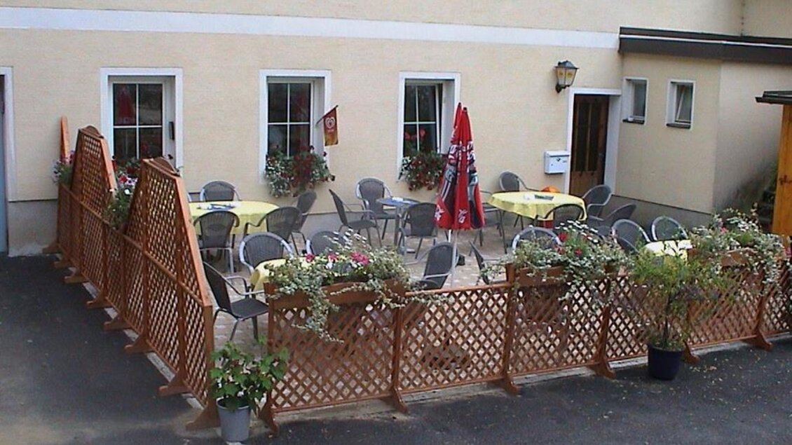 Eine einladende Terrasse mit gelben Tischen und Stühlen, umgeben von Blumen. Im Hintergrund befindet sich ein helles Gebäude mit Fenstern. | © Gasthaus Krapinger