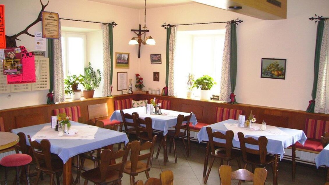 Ein gemütliches Restaurant mit Holztischen und -stühlen. Die Wände sind mit Pflanzen und Bildern dekoriert, und Tageslicht strömt durch die Fenster. | © Gasthaus Krapinger