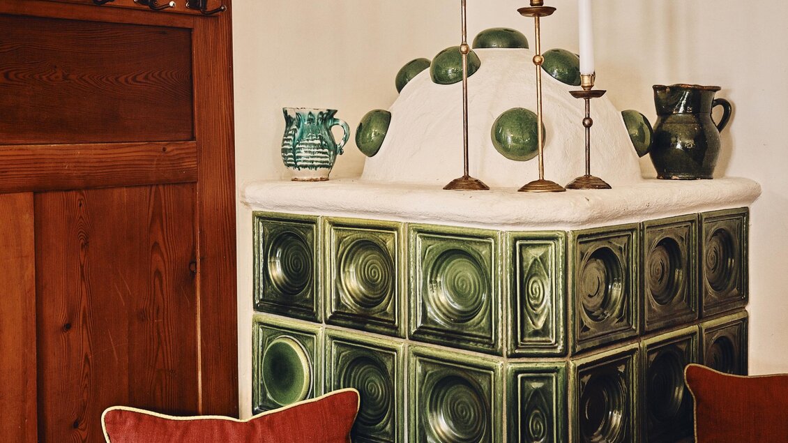Ein gemütlicher Essbereich mit einem Kachelofen in Grüntönen. Der Tisch ist für das Essen gedeckt, mit eleganten Servietten und Kerzenhaltern. | © Armin Walcher
