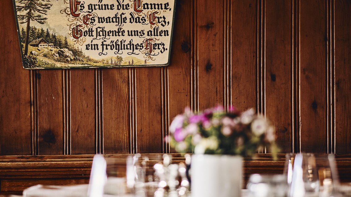 Ein rustikales Restaurant mit Holzwänden und einem dekorativen Schild. Auf dem Tisch stehen Blumen und Gläser für die Gäste. | © Armin Walcher