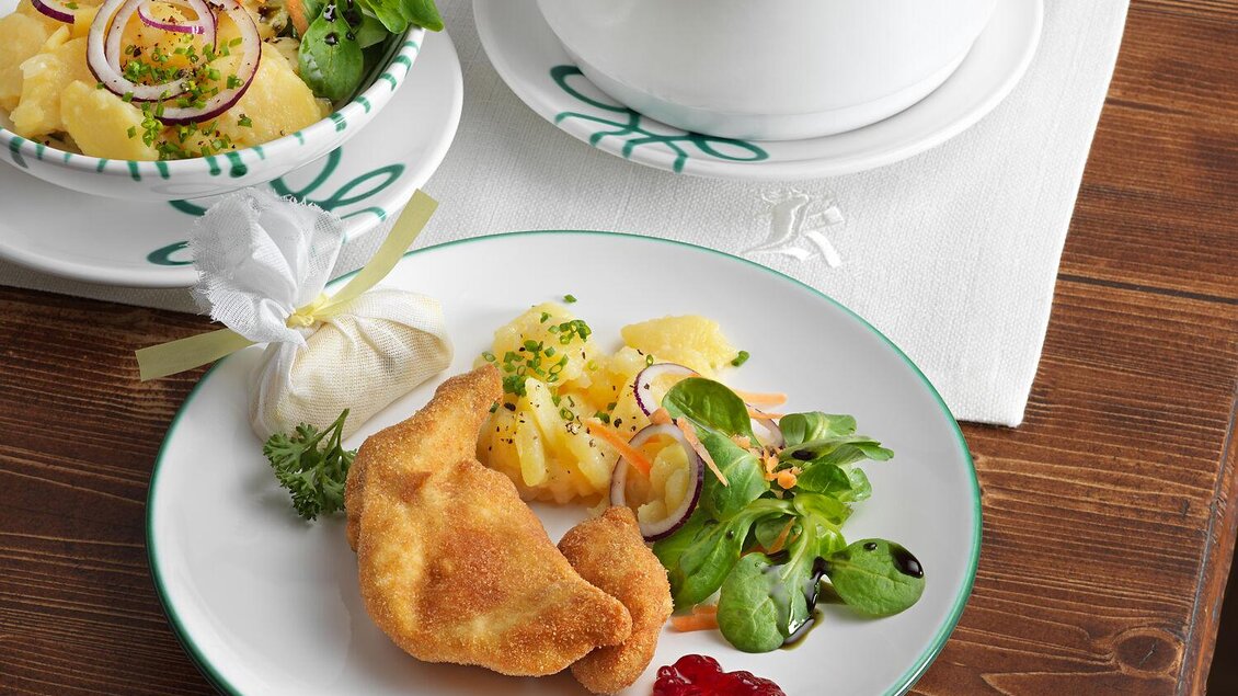 Ein Teller mit gefüllten Teigtaschen, frischem Salat und einer Beilage aus Kartoffeln. Daneben steht eine Schüssel mit weiteren Teigtaschen und einer kleinen Portion Soße. | © TAUROA GmbH