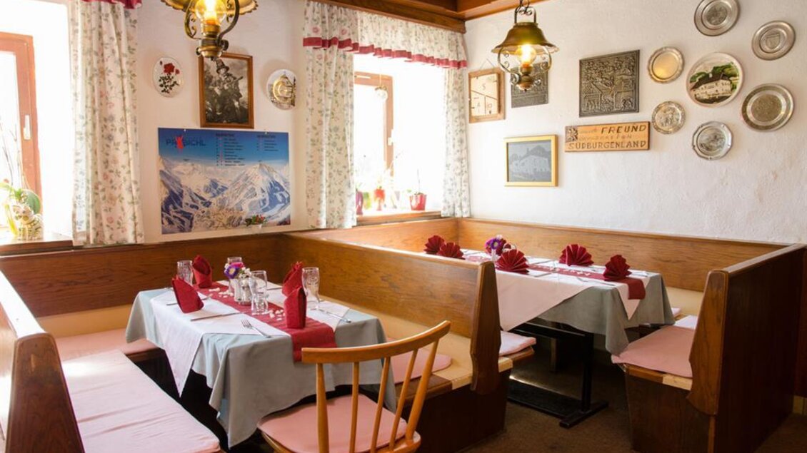 Ein gemütliches Restaurant mit Holzmöbeln und blauen Tischdecken. An den Wänden hängen Bilder und dekorative Teller. | © Gasthaus Langreiter