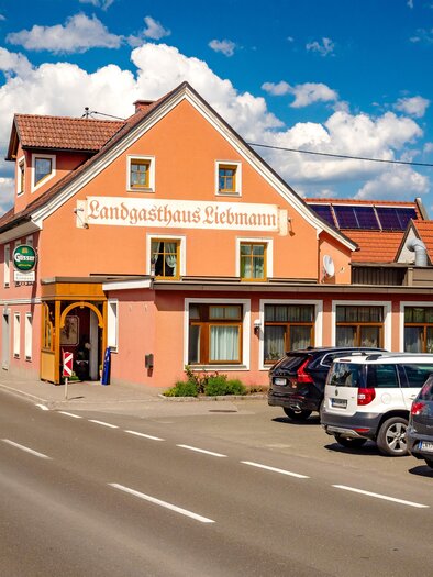 A cozy inn with an orange facade, surrounded by cars and a clear sky. The road runs directly past the building. | © Wolfgang Speckner