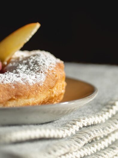 A delicious donut dusted with powdered sugar and fresh fruit on a plate. The background is soft and blurred, which highlights the pastry. | © © 2022 Alwin Strasser - strasserconcept