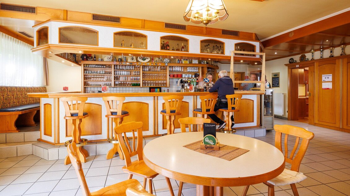 Ein gemütliches Restaurant mit einem Holzbar und mehreren Stühlen. Im Vordergrund steht ein runder Tisch mit einem kleinen Gegenstand darauf. | © TV Region Graz - Harry Schiffer