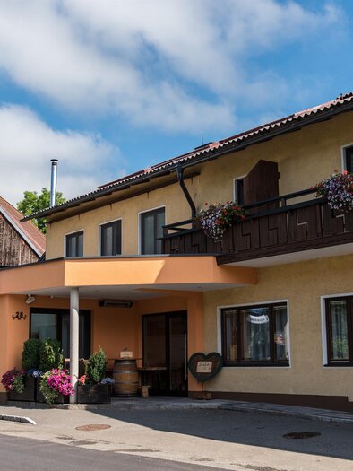 Ein charmantes Gasthaus mit einer einladenden Fassade und bunten Blumen. Im Hintergrund ist ein traditionelles Gebäude zu sehen. | © Gasthaus Mossauer