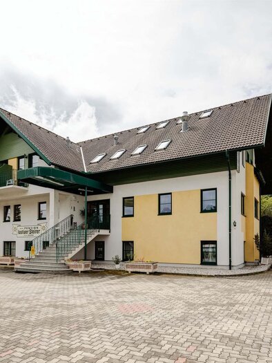 A modern building with two stories and an inviting entrance. Surrounded by a landscaped area and a parking lot. | © M. Meieregger