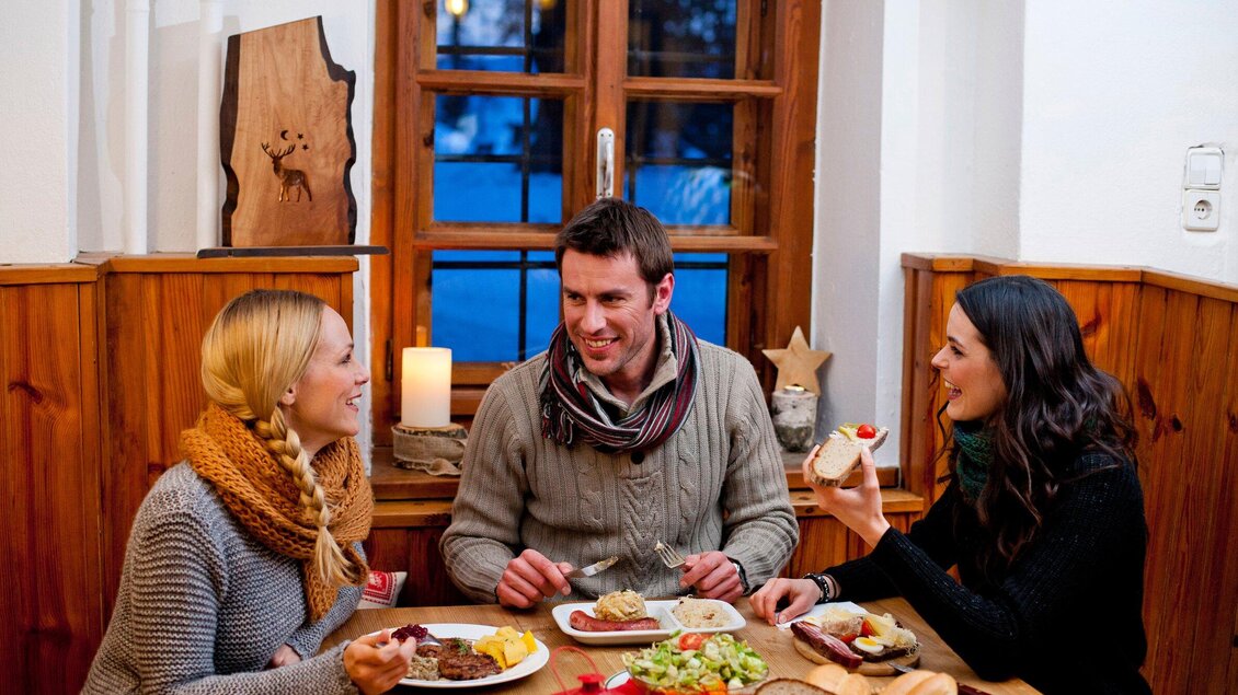 Drei Freunde genießen eine Mahlzeit in einem gemütlichen Restaurant. Der Tisch ist mit verschiedenen Gerichten und frischen Salaten gedeckt. | © Region Graz - Tom Lamm