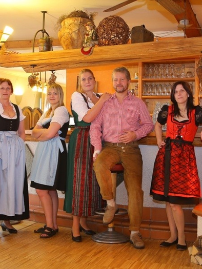 Eine Gruppe von sechs Personen in traditionellen Trachten steht in einem gemütlichen Restaurant. Im Hintergrund ist ein Kamin und eine rustikale Einrichtung zu sehen. | © Gasthaus Ruckenstuhl