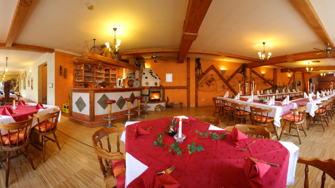 Ein einladendes Restaurant mit Holzmöbeln und roten Tischdecken. Im Hintergrund befindet sich eine Bar und eine gemütliche Atmosphäre mit warmem Licht. | © Gasthaus Ruckenstuhl