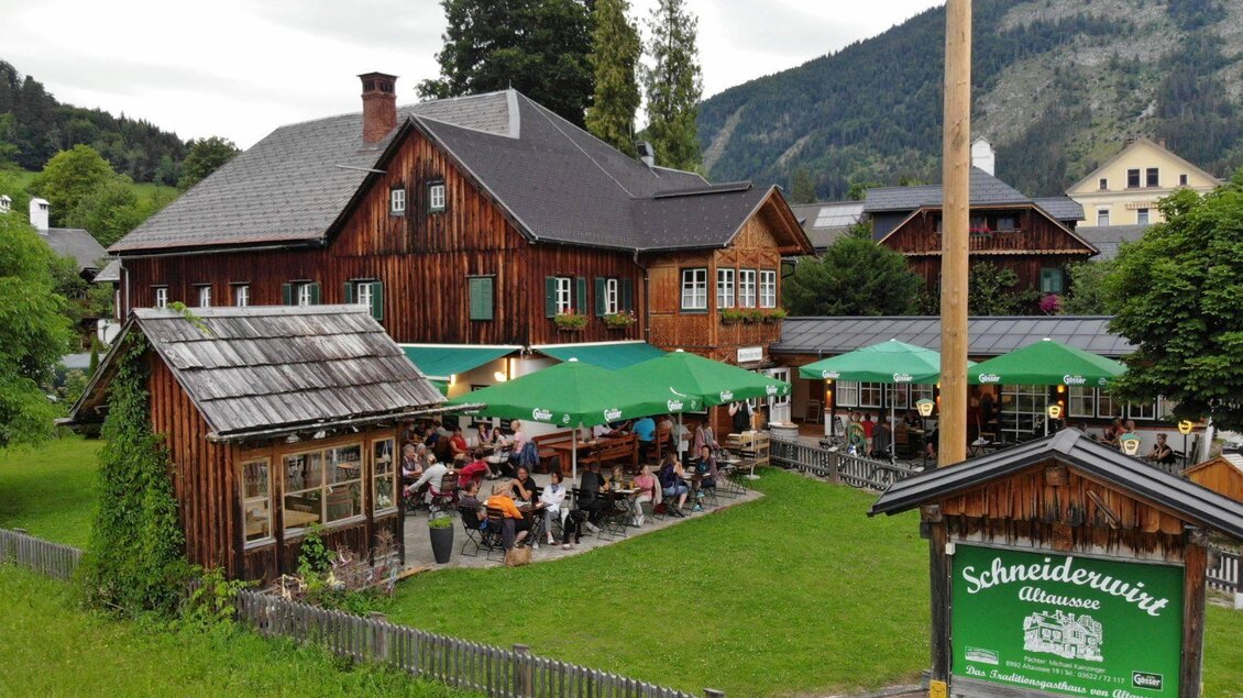 Ein gemütliches Restaurant mit Außenplätzen und grünen Schirmen. Im Hintergrund sind Berge und Bäume zu sehen. | ©  Schneiderwirt_Kainzinger