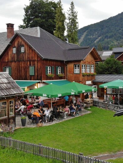 Ein gemütliches Restaurant mit Außenplätzen und grünen Schirmen. Im Hintergrund sind Berge und Bäume zu sehen. | ©  Schneiderwirt_Kainzinger